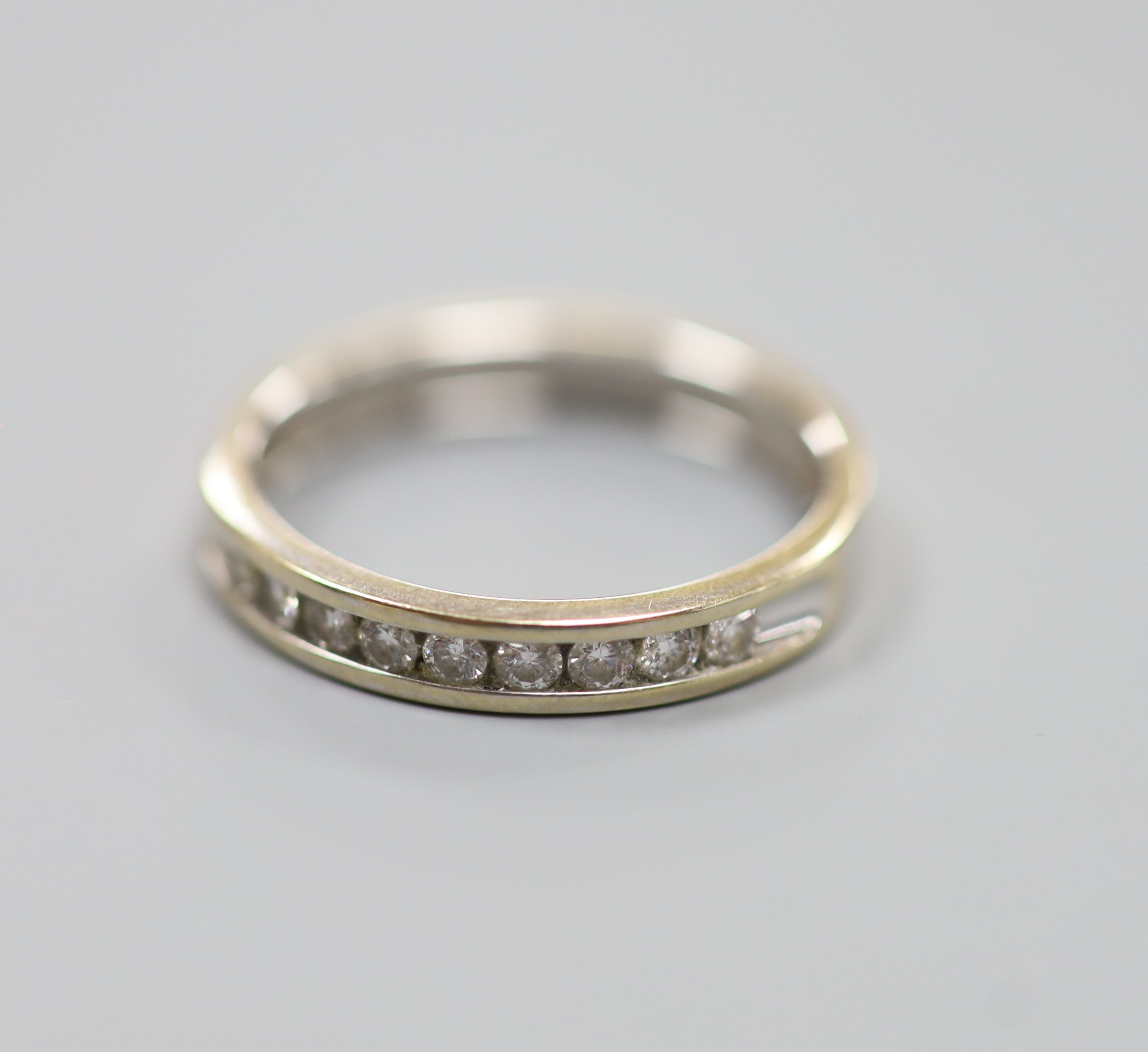 A modern 18ct white gold (worn) and nine stone channel set diamond half eternity ring, size P